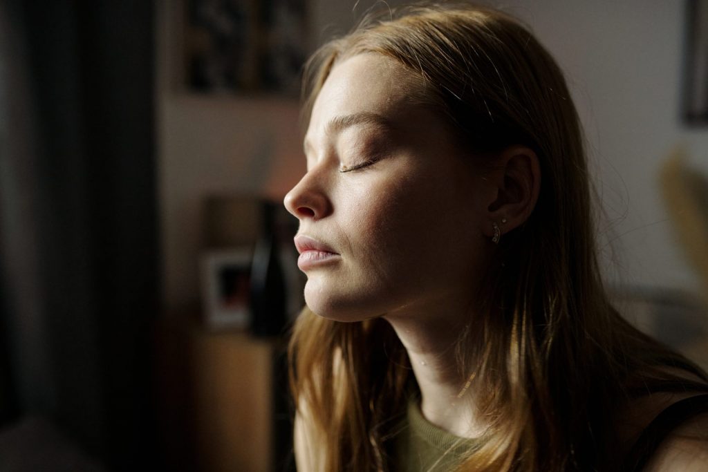 Frau mit geschlossenen Augen atmet im warmen Fensterlicht durch – Burnout-Coaching in München-Pasing